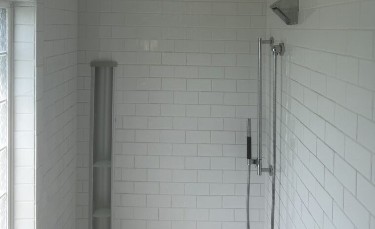 A modern walk-in shower featuring white subway tile, a ceiling-mounted square chrome rain shower head, and a wall-mounted hand-held sprayer attachment.
