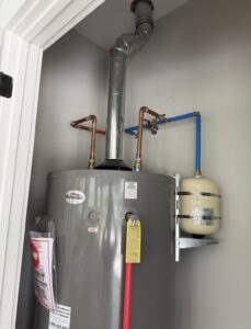 Professional installation of a Richmond gas water heater featuring a thermal expansion tank secured by a side-mounting bracket, rigid copper piping transitioning to blue PEX piping, and a properly pitched gas vent for safe combustion gas removal.