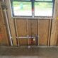 Framed wall with drain arm, PEX water lines, and a handwritten note on wooden stud framing.