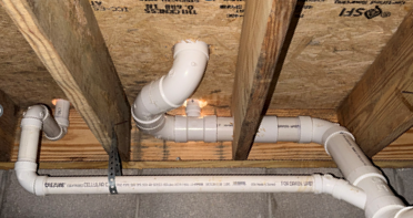 Overhead perspective showing neat PVC drain branches and strap hangers under crawlspace subfloor.