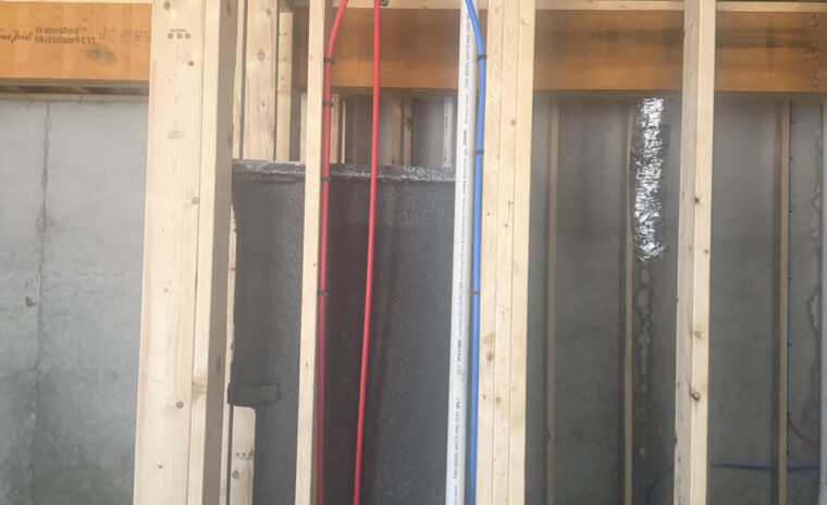 Shower rough-in framing showing red and blue PEX lines connected to a brass mixing valve with PVC vent.