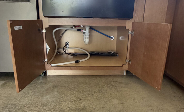 Apron-front farm sink installation showing PEX lines, tailpiece drain, and dishwasher discharge hose connection.