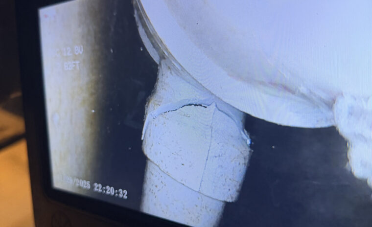 Sewer inspection camera screen revealing a cracked PVC sanitary tee hidden inside a wall cavity.