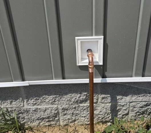 Exterior copper water heater T&P safety relief discharge pipe terminating downward through house siding.