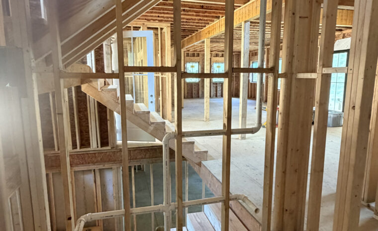 Wood-framed multi-story home under construction showing PVC drain and vent stack rough-in piping running through wall studs between floor levels.
