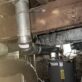Double-wall B-vent flue line elbow connection routed from a Rheem gas water heater in the basement up through floor joists.