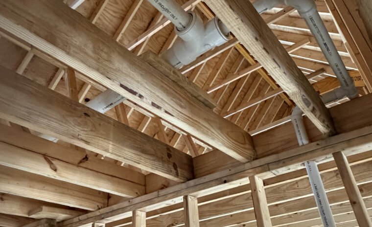 Clean PVC DWV pipe rough-in with aligned manufacturer lettering running through wooden roof trusses.