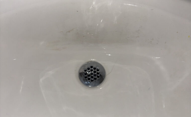 Newly installed chrome grid strainer drain body mounted in white porcelain sink basin.