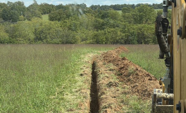 Wide field view of completed underground water line backfill and livestock watering station.