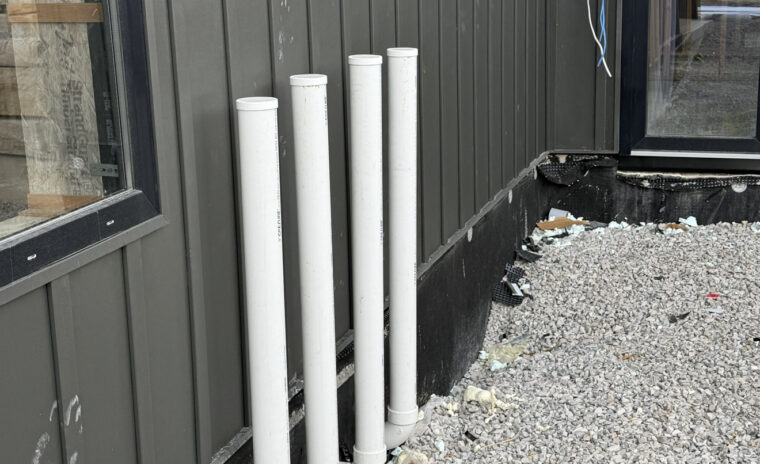 Exterior wall of custom build showing four 3-inch PVC water heater vent pipes extending neatly through wall.