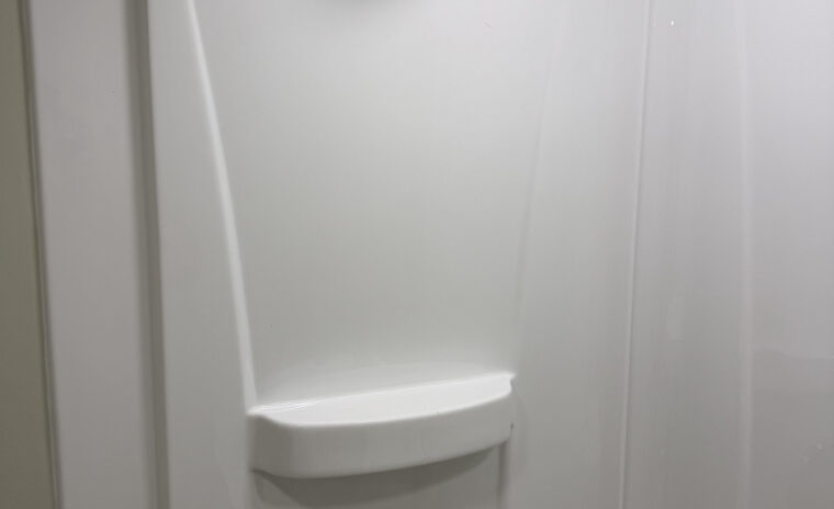 Single-handle brushed nickel faucet mounted on a white vanity top next to a modern stall shower.