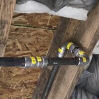 155cfe81 8f23 482b b925 01b1933bd3ed 53c34e2a 3996 4b18 a866 b5b079bf34a6 Threaded black iron gas pipe secured to wooden floor joists with multiple 90-degree fittings and yellow identification tags for code compliance