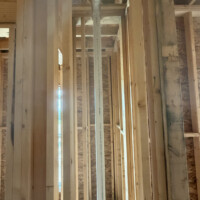 785FF4C6 F4F9 46E2 821C B60DA3A97E15 0f928e99 558a 48cd afdb 80484ca95450 Looking up at a web of architectural roof framing where a white PVC drain line runs horizontally across the ceiling before bending up toward the roofline.