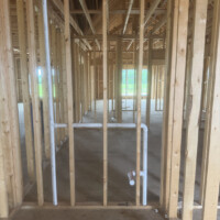 7D56147B BBA7 4E83 8FAC 0BEFEF4ECD3D 1748a98a f0c4 47dc aa9e 3e2366a6f9c7 Upward view looking into open ceiling joists and roof trusses showing a long horizontal PVC plumbing pipe cleanly sloped and supported through structural timbers.