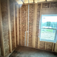 8DEA7DE0 CD6B 4797 A0C9 F35C66A14485 638b82aa bdef 4fa7 9486 302f29905bdb Wall cavity with neatly installed vertical PVC vent line running up through ceiling framing.