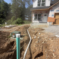 C6129774 E631 4CFF 8D0B 152482CDA18E 9bc944b5 c5cd 44b0 96e5 be26562a659e o Image 3 (Wide site layout): High-angle shot of a construction site showing the white sewer lateral pipe snaking through a trench toward a green utility riser cap