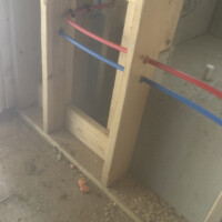 DDA6F09E 4B1E 4128 B85D DEE232C1B5C1 19b0d4e4 9f84 42f1 927a 2cc6f671461d Red and blue PEX water supply lines routed horizontally through wood wall studs during the rough-in plumbing stage for a bathroom remodel.