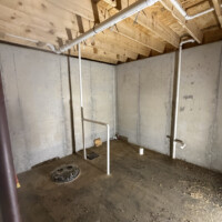 E2CD6E69 18CE 4C8C A235 ED950F92677C 60b4aaa9 b564 4fc7 a384 f2e975f1fafd Basement foundation wall with sump basin, overhead main drain line, and vertical vent stack.