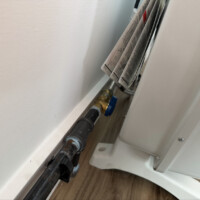 ReactNativeBlobUtilTmp 0w4sz11pwqjsfmg7wz4lrvw Black iron gas pipe with a blue dedicated shut-off valve installed behind a white wall heater.