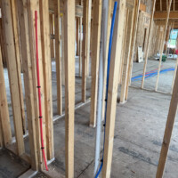 ReactNativeBlobUtilTmp 28gyiiv76zee6wqzg6efge Wall framing with vertical PVC vent pipe and color-coded red and blue PEX water lines.
