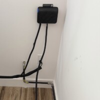 ReactNativeBlobUtilTmp 7beuqmlmu1u5v592jf5p Interior black iron gas line installation running along the baseboard and around a corner, positioned below a black electronic device mounted on the wall.