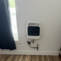 ReactNativeBlobUtilTmp 9m97uvp7d4b7bp6h5oskes Wall-mounted white gas heater showing the black iron gas line and blue shut-off valve connection.