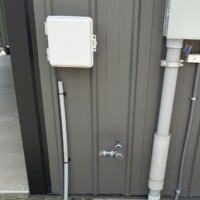 ReactNativeBlobUtilTmp h0gouhwfpf7d0pq0swd1zs Exterior gas line stub-out on gray metal siding, located near a white Spectrum box and electrical conduit.