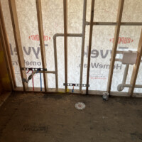 ReactNativeBlobUtilTmp tb6jmjsh82qlyp088724j Bathroom wall framing with toilet flange on subfloor, vanity drain piping, and vertical vent stack.