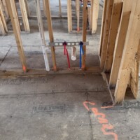 ReactNativeBlobUtilTmp zadooz30oxh0tfop9wplw Framed partition wall with sink drain rough-in and PEX water lines secured to mounting bracket.