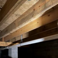Screenshot 2026 07 25 070701 Galvanized hanger straps securing long-run DWV piping underneath floor joists in a home crawlspace.