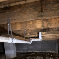 Screenshot 2026 07 25 074242 Well-supported long-run PVC waste pipe with metal hanging straps running above a crawlspace dirt floor.