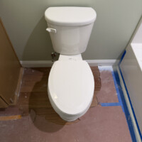 ReactNativeBlobUtilTmp 13k79z90x28vfdxipkc54i Newly installed white Gerber toilet in a finished bathroom with protective floor paper.