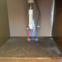 ReactNativeBlobUtilTmp 2y2nvwqkdes0spbz82d61n Clean under-sink vanity cabinet plumbing with color-coded PEX water supply lines and a white PVC drain trap.