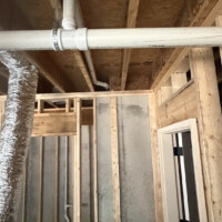 ReactNativeBlobUtilTmp 705jpjyhqxhljhpv2ml3w Tub enclosure framing showing a vertical PVC vent pipe offset with flexible HVAC ducting visible in the background.