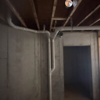 ReactNativeBlobUtilTmp 8jz1pb3776yvj8xaokfsh Main PVC drain line routed parallel to a large sheet metal HVAC trunk line in basement ceiling framing.