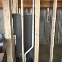ReactNativeBlobUtilTmp b22zqgbz3fpupmzbb92jqo Tub enclosure framing showing a vertical PVC vent pipe offset with flexible HVAC ducting visible in the background.