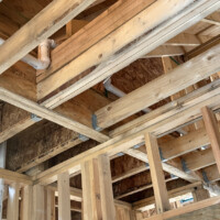 ReactNativeBlobUtilTmp bg4qixhgj8tpmguvrx2e4o Overhead view of PVC drainage piping with aligned lettering passing through ceiling joists.