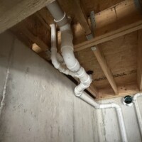 ReactNativeBlobUtilTmp bxw2z7kbnssv094y7ij9 Overhead PVC drain line assembly neatly angled through floor joists above a basement wall alongside HVAC penetrations.