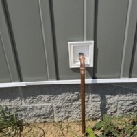 ReactNativeBlobUtilTmp gar25gyb95j9xom3jii7sb Exterior copper water heater T&P safety relief discharge pipe terminating downward through house siding.