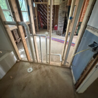 ReactNativeBlobUtilTmp gyyaltt0s2bt4gjyv0ath7 Rough-in plumbing view showing PVC drain pipes, toilet flange, and PEX water lines in wall framing during a full overhaul.
