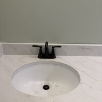 ReactNativeBlobUtilTmp ifbv2550raxsgnn0ostj Oil-rubbed bronze lavatory faucet trim detail on a solid surface vanity top.