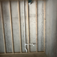 ReactNativeBlobUtilTmp iqictip7i9pzm4xbfs547 Basement stud framing featuring a vertical PVC drain line alongside a metal HVAC vent pipe penetration.