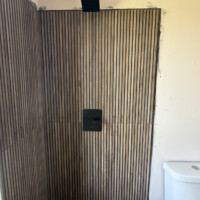 ReactNativeBlobUtilTmp j0hhice8nw6ncg6mqajbd Modern matte black shower valve trim and square rain showerhead installed on wood-slat accent wall.
