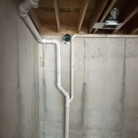 ReactNativeBlobUtilTmp mrnj5q0drr90e77j27vg Overhead PVC drain pipe installed tight against floor joists right above rectangular metal HVAC ductwork.