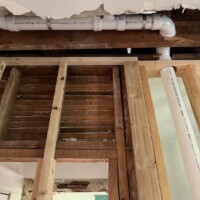 ReactNativeBlobUtilTmp nj4tlgrn0nfqo3xprbwyk Upclose view of PVC waste pipe suspended above framed wall and original wood framing.