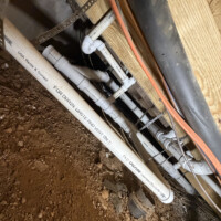 ReactNativeBlobUtilTmp p3ikf0pf1dwrsvisq7rml Tight crawl space view showing multiple PVC drain branches secured to joists with metal perforated strapping.