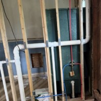 ReactNativeBlobUtilTmp vu0ph978cobfooms839wi Interior bathroom rough-in showing vertical PVC stacks, PEX lines, and toilet flange in opened floor framing.