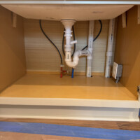 ReactNativeBlobUtilTmp xfnfhxzp7wbxwzcz5r1jso Under-sink vanity drain connections and chrome angle stops inside a custom vanity cabinet.