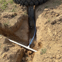 ReactNativeBlobUtilTmp 3klqigh8w13h17kirlmlfp Excavated trench showing underground water supply pipe connecting to frost-proof yard hydrant base.