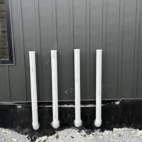ReactNativeBlobUtilTmp c0ftooml2waafko9cweptq Exterior wall of custom build showing four 3-inch PVC water heater vent pipes extending neatly through wall.